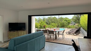 Un soggiorno moderno con una grande TV, un divano verde acqua, un'area pranzo con vista piscina e posti a sedere all'aperto.