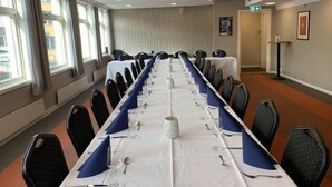 Una sala de conferències amb una taula llarga preparada per a una reunió, equipada amb cadires, taules i un mantell de taula blanc.
