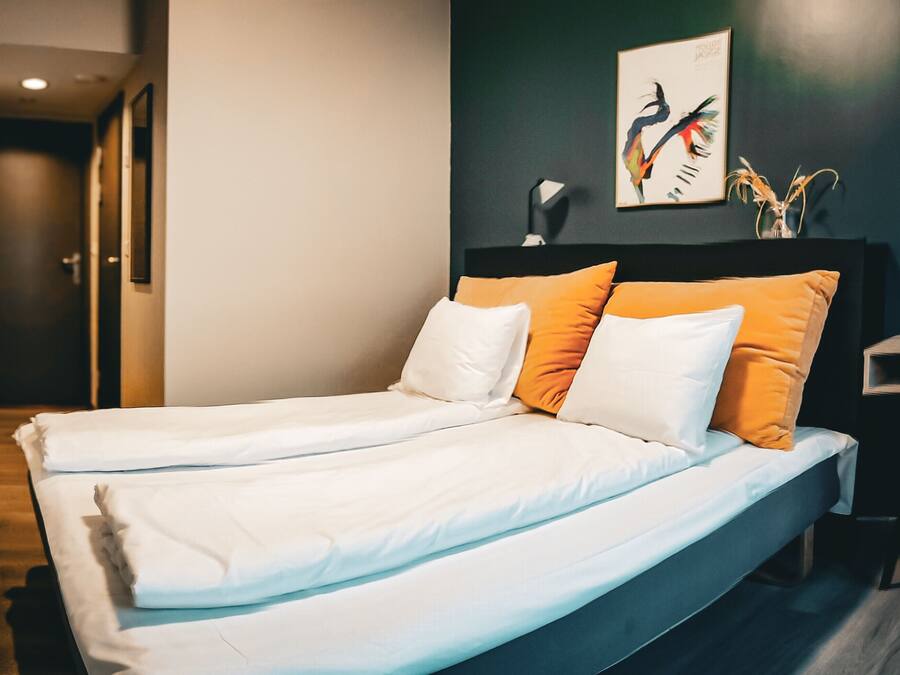 Una moderna camera d'albergo con un letto grande, due cuscini, un comodino e un'opera d'arte appesa al muro.