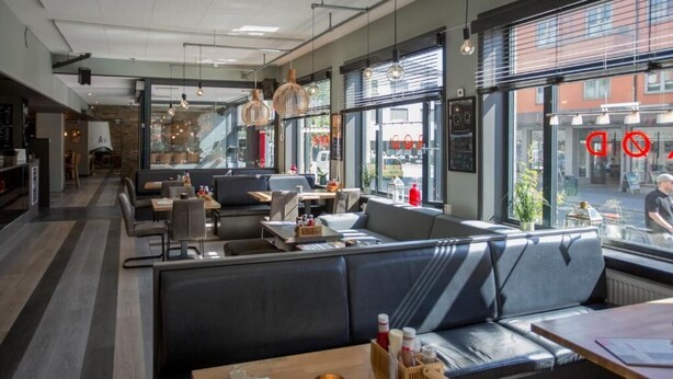 Un restaurant modern amb una zona de seients acollidora, grans finestres i vista al carrer.