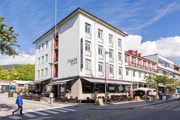 A hotel with a modern facade, outdoor seating area, and a pedestrian crossing.