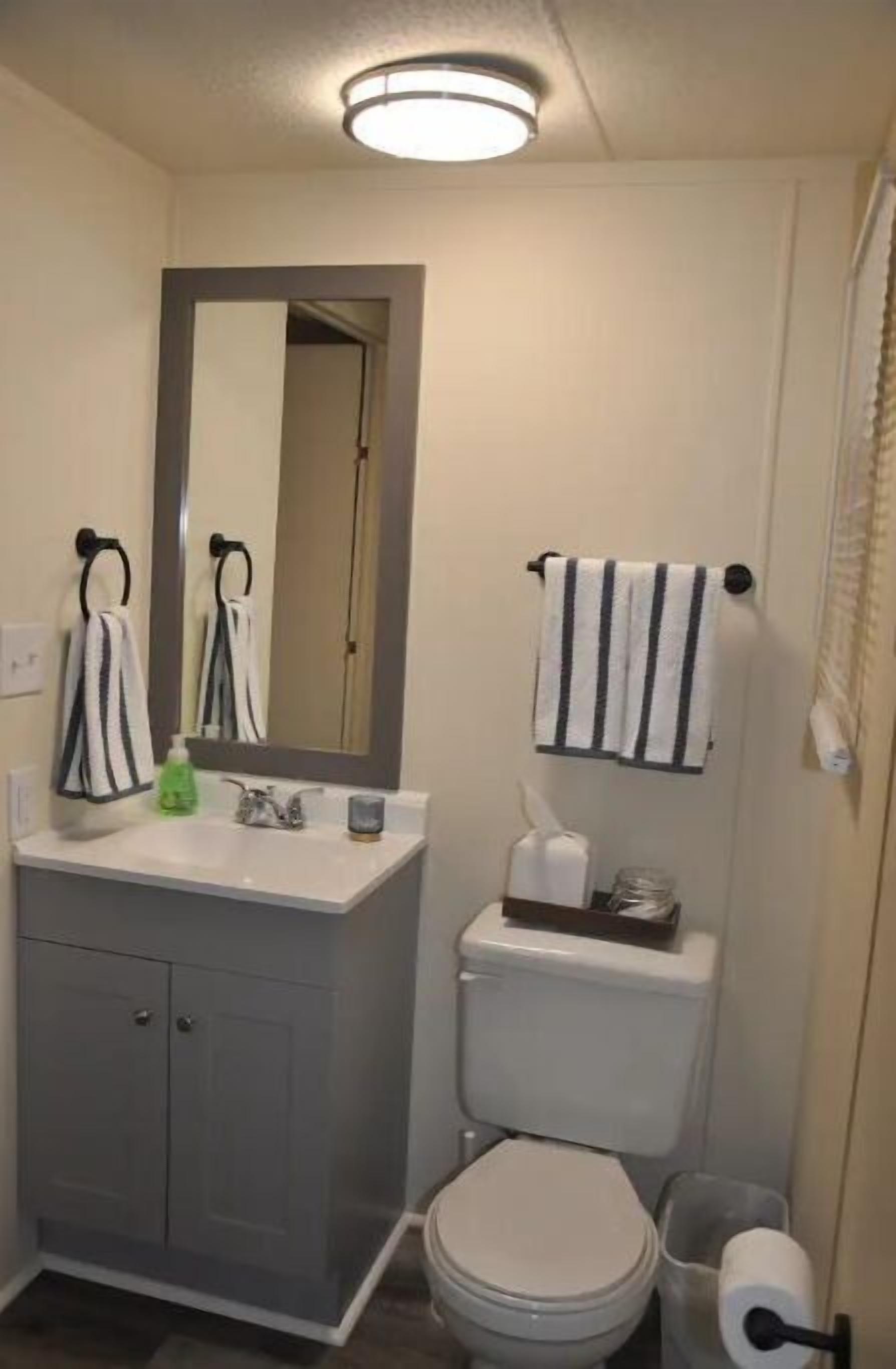 Un baño con inodoro, lavamanos y espejo. Hay dos toallas colgadas en barras para toallas.