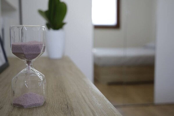 An hourglass on a wooden surface with a plant and a window in the background.