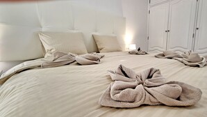Ein ordentlich bezogenes Bett mit Handtüchern, die zu einer Schleife geformt sind, ein Nachttisch mit Lampe und ein Kleiderschrank mit Doppeltüren.