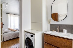 Relax in a clean and minimalist space with a neatly made bed, washing machine, and a separate bathroom area.