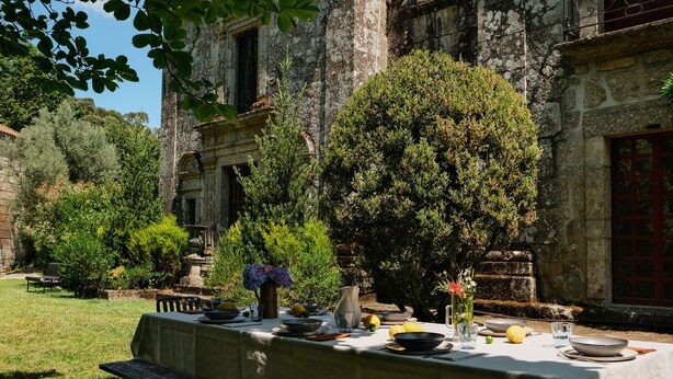 Un'area pranzo all'aperto con un tavolo apparecchiato per due, circondata dal verde e con un edificio in pietra sullo sfondo.