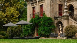 Un edificio storico con infissi rossi, una statua e posti a sedere all'aperto con ombrelloni.