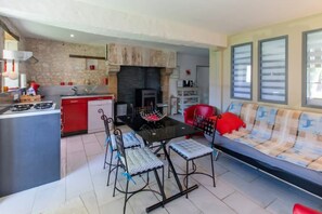 A modern kitchen with a gas stove, red cabinets, and a dining area with a black table and metal chairs. - Vacances au Guimapé bis Gite Paisible de Campagne (Assay)
