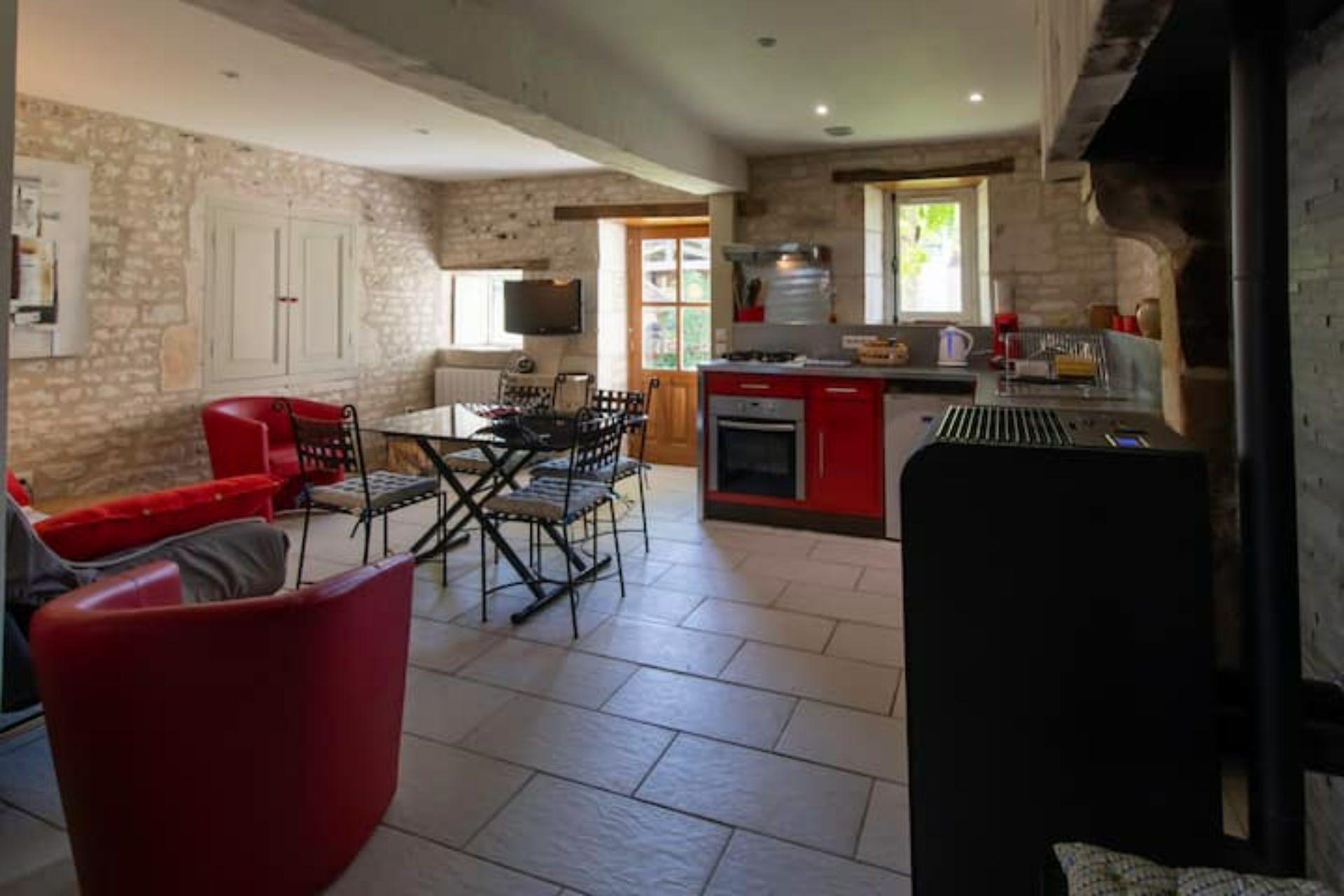 A spacious kitchen with a dining area, stone walls, and a red dining set.