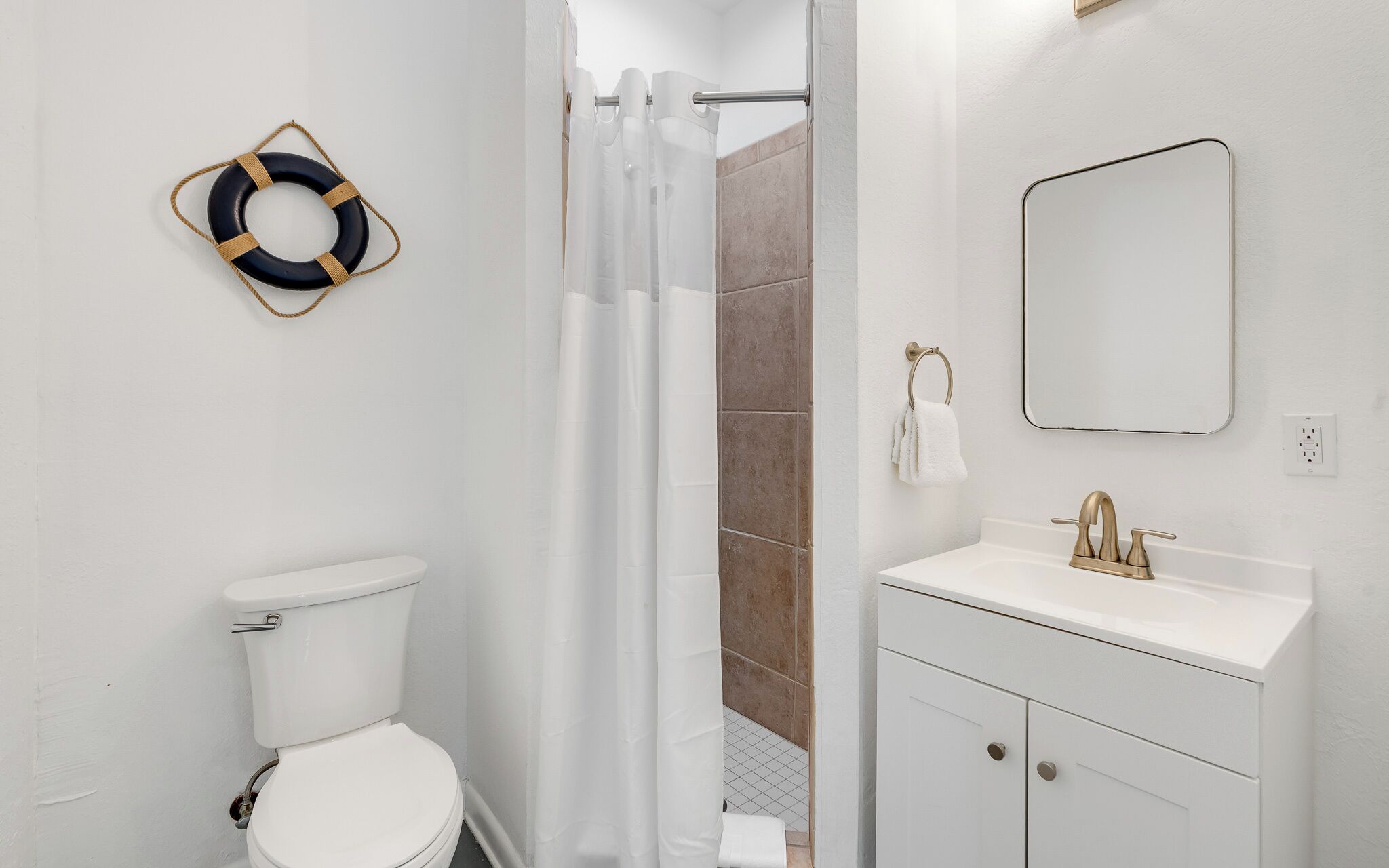 Une salle de bain équipée de toilettes, d’un lavabo avec un miroir, d’un rideau de douche et d’une bouée de sauvetage accrochée au mur.