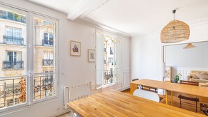 Un comedor con mesa y sillas de madera, ventanas amplias con balcones y una lámpara colgante.