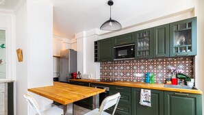 Una cocina moderna con armarios verdes, encimera de madera y sillas blancas.