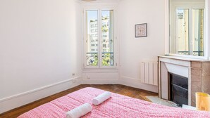 Una habitación con un ventanal grande, una chimenea y una colcha rosa.