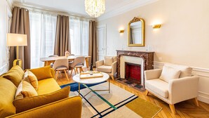 Un salon bien éclairé, doté d’une cheminée, d’un coin repas et d’un lustre.