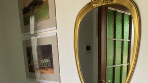 Quarto com cômoda de madeira, espelho com moldura dourada e duas fotos emolduradas na parede.