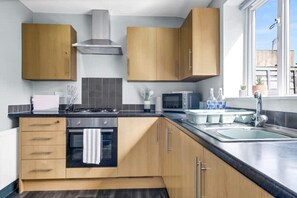 Une cuisine moderne avec des armoires en bois, une hotte de cuisinière en acier inoxydable, un four encastré, un four à micro-ondes et un évier avec un robinet.