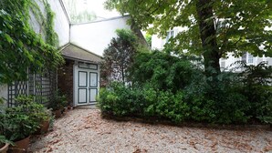 A gravel courtyard with a white door, surrounded by dense greenery and a brick wall. - GuestReady - Minimalist stay near Opéra Bastille (Paris)