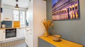 Een moderne keuken met witte kasten, een inbouwoven en een raam. Op het aanrecht staat een vaas met gedroogde bloemen.