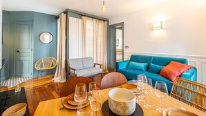 Een eetgedeelte met een houten tafel voor vier personen, een blauwe bank en een rieten stoel.