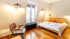 Een slaapkamer met een houten vloer, een bed met oranje kussens, een stoel en twee wandlampen.