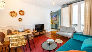 Een woonkamer met een bank, televisie, eettafel en stoelen.
