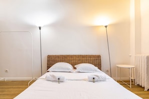 Cama bem arrumada com almofadas e toalhas, uma mesinha de cabeceira, um abajur e um radiador.