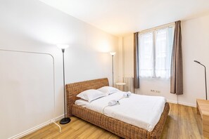 A room with a wicker bed, a standing floor lamp, a radiator, and a window with curtains.