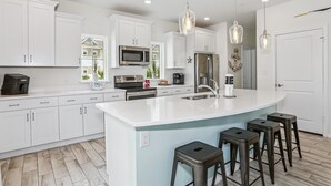 A modern kitchen with white cabinetry, stainless steel appliances, and a large island with bar stools. - Beautiful house at Lost Key Resort Perdido Key (Perdido Key)