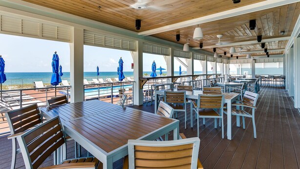 A covered outdoor dining area with wooden tables and chairs, overlooking a pool and beach. - Beautiful house at Lost Key Resort Perdido Key (Perdido Key)