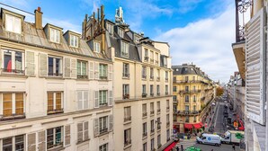 Une vue de rue sur des immeubles parisiens, avec un café et une pharmacie.