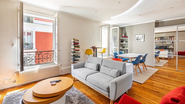 Un salon moderne avec un canapé gris, une table basse en bois et un coin repas avec des chaises bleues.
