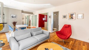 Un salon moderne avec un canapé gris, un fauteuil rouge et un coin repas comprenant une table et des chaises.
