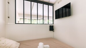 A small, clean room with a bed, a window with bars, a mounted TV, and a power outlet on the wall. - GuestReady - Peaceful Haven in Gare (Paris)