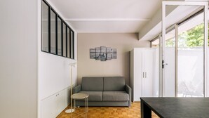 A compact living space with a grey sofa, a small round table, and a cabinet. - GuestReady - Peaceful Haven in Gare (Paris)