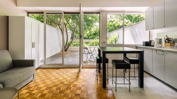 A modern kitchen with a dining area, large sliding glass doors leading to a deck, and a grey sofa. - GuestReady - Peaceful Haven in Gare (Paris)