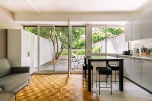 A modern kitchen with a dining area, large sliding glass doors leading to a deck, and a grey sofa. - GuestReady - Peaceful Haven in Gare (Paris)