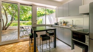 A modern kitchen with a dining area, large windows, and a view of greenery. - GuestReady - Peaceful Haven in Gare (Paris)