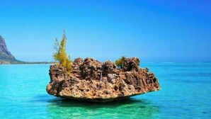 Ein klares, blaues Meer mit einer felsigen Insel im Vordergrund und einem Berg im Hintergrund.