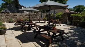 An outdoor patio with picnic tables and umbrellas, surrounded by stone walls and potted plants. - George and Dragon Clifton (Penrith)