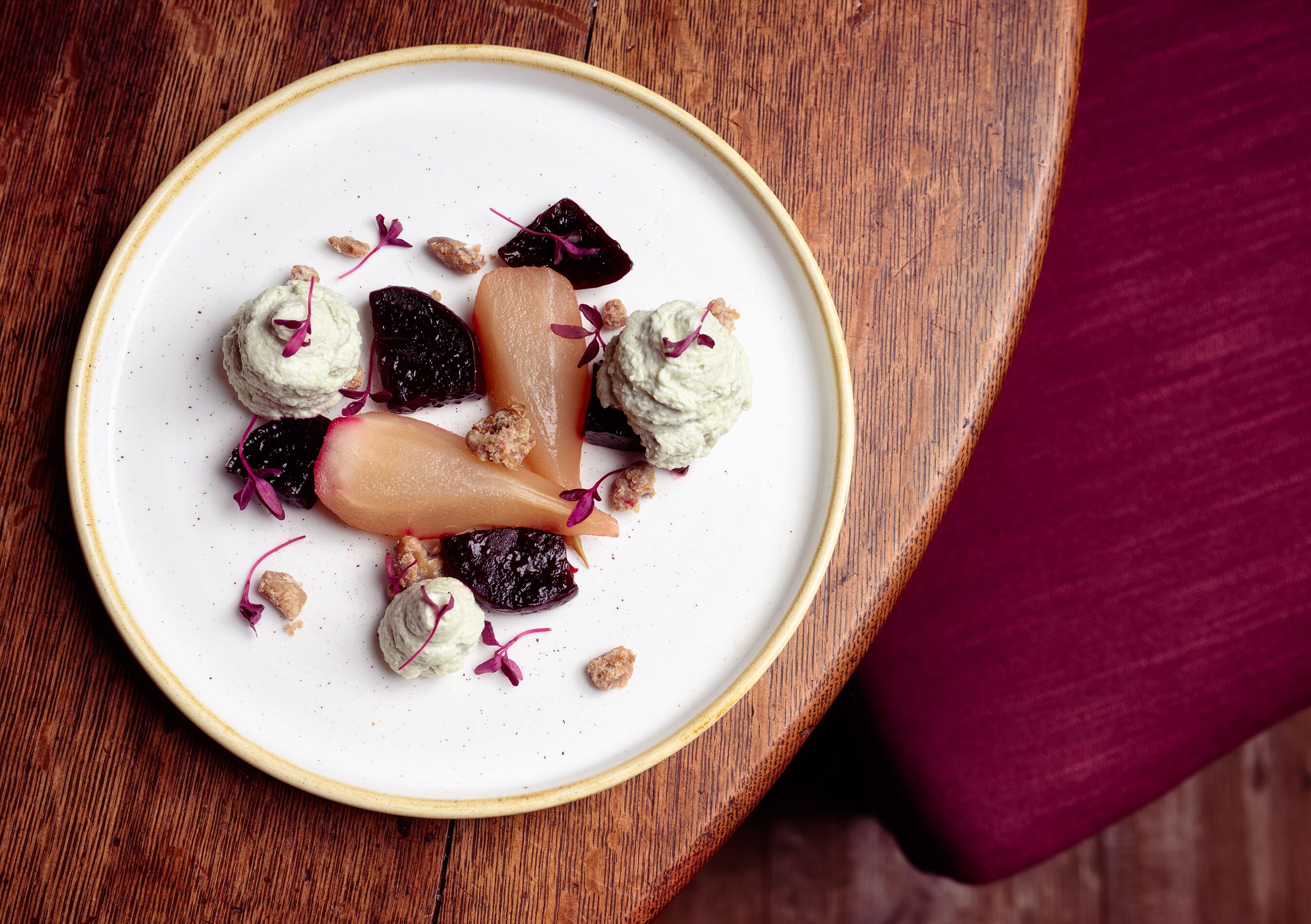 A white plate with a variety of food items, including what appears to be a pear, some berries, and a dollop of cream, on a wooden surface.