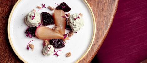 A white plate with a variety of food items, including what appears to be a pear, some berries, and a dollop of cream, on a wooden surface.