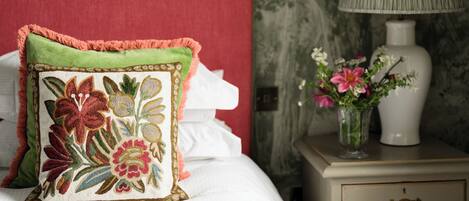 A neatly made bed with a red headboard, a decorative pillow, a bedside table with a lamp and a vase of flowers.