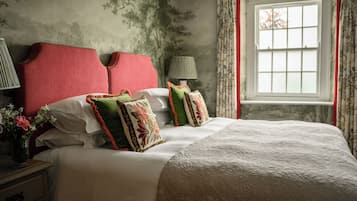 A bedroom with a large bed, floral-patterned pillows, a red headboard, and a window with curtains.