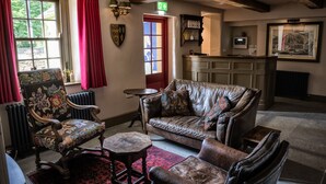 A cozy room with a leather sofa, matching armchairs, and a small table. A red door and a window with curtains are visible. - George and Dragon Clifton (Penrith)