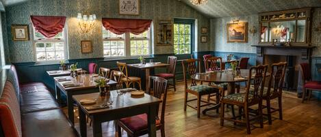 A dining area with wooden tables and chairs, a bench, and a fireplace.