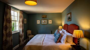 Um quarto com cama, duas luminárias de cabeceira, uma cadeira e uma janela com cortinas.