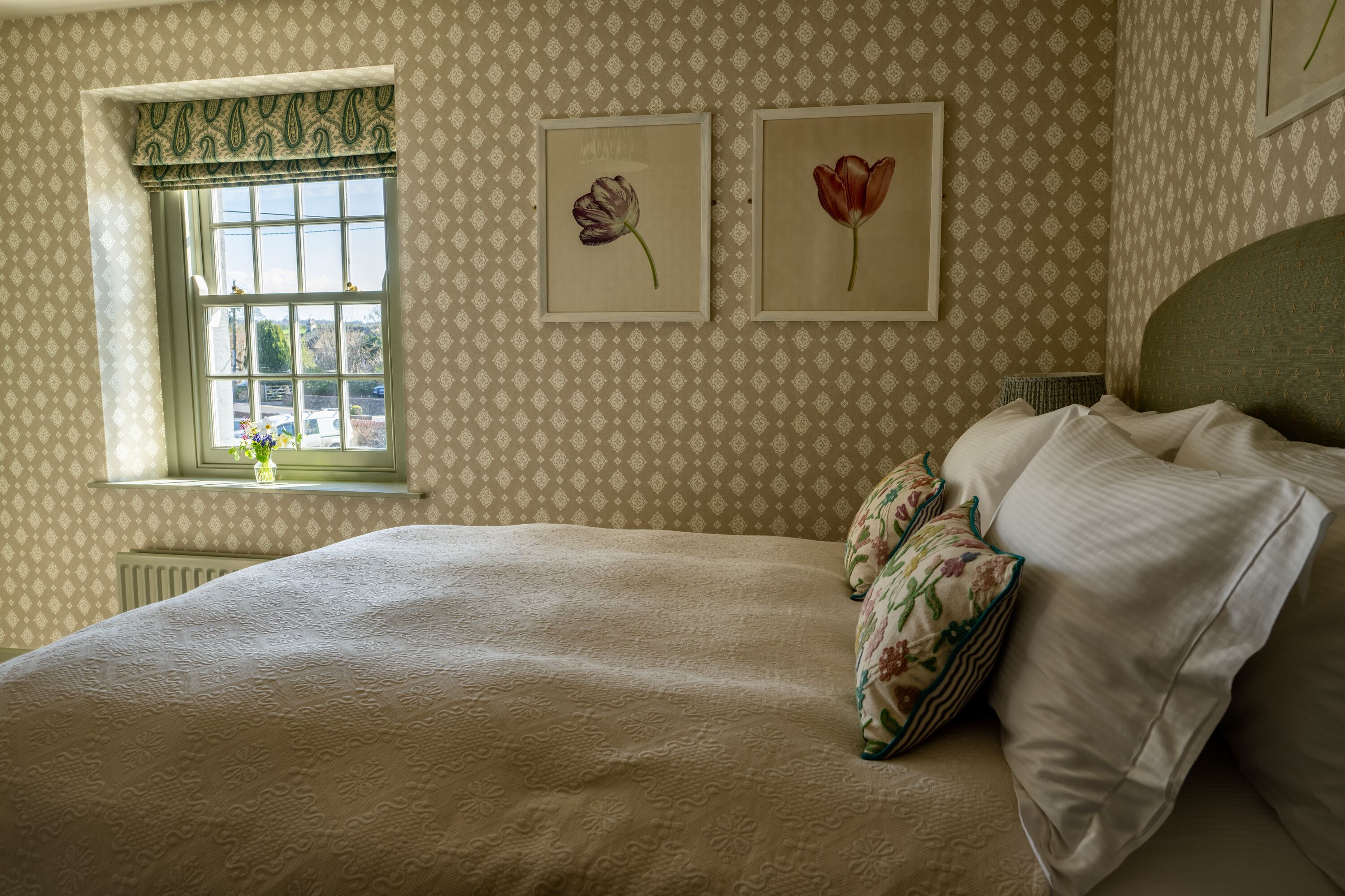 A bedroom with a large bed, a window with a view, and two framed pictures on the wall.