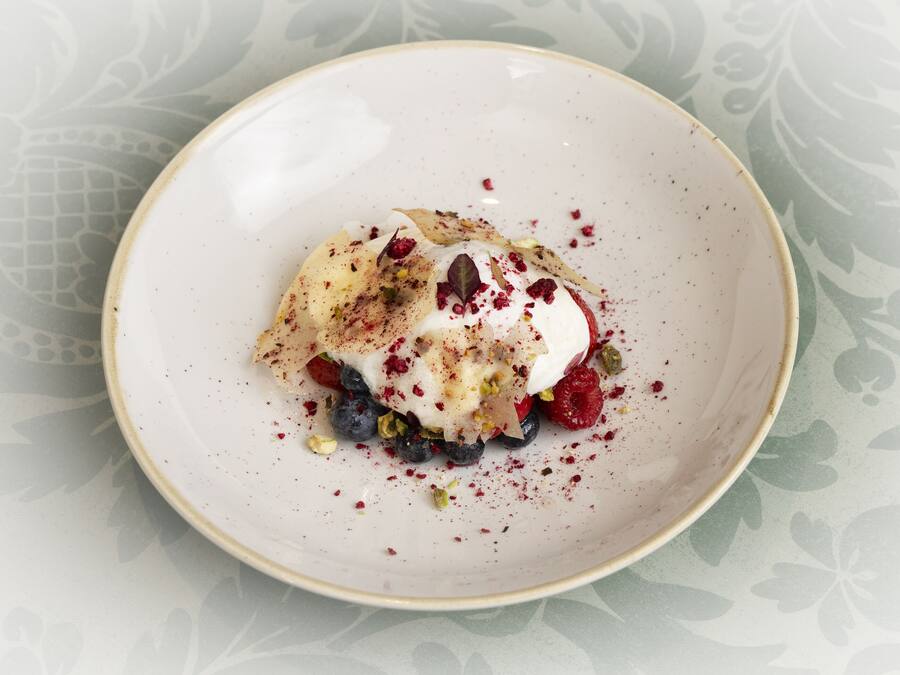 A dessert on a plate with berries and nuts.