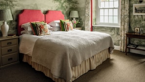 A bedroom with a large bed, a nightstand, a lamp, a window with curtains, and a wall with a tree mural. - George and Dragon Clifton (Penrith)