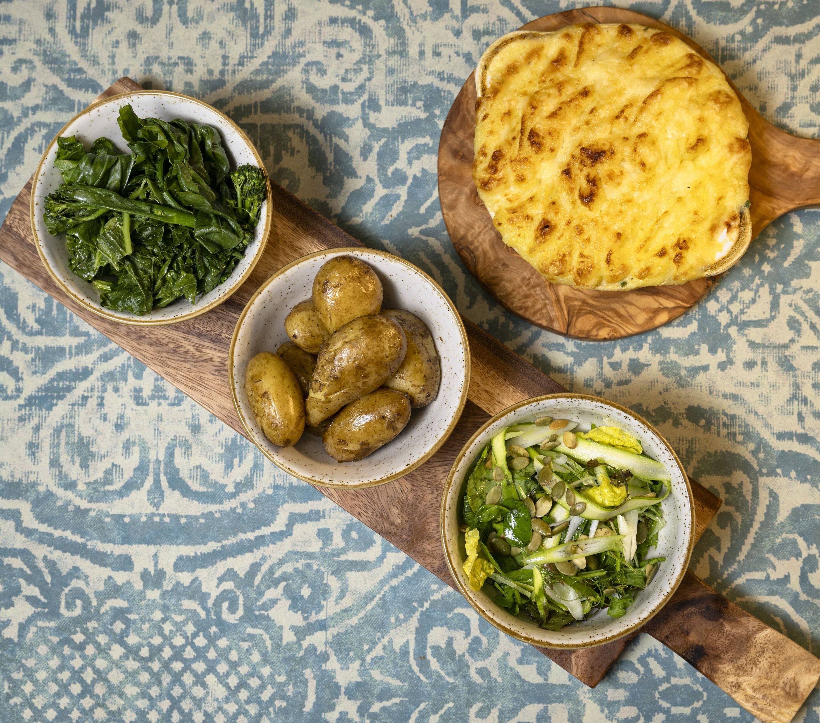 A table with various dishes including leafy greens, potatoes, flatbread, and a salad with nuts.